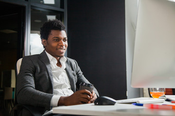 Hardworking smiling afroamerican at office look at computer monitor. Young handsome black man student do his job