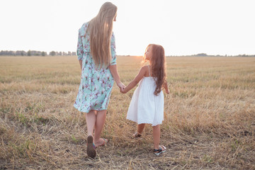 Happy healthy family concept. A young beautiful woman with her little cute daughter walking in the wheat gold field on a sunny summer day. Parents and kids relationship