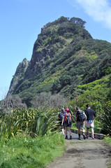 Group of unrecognizable young people hiking in KareKare beach New Zealand
