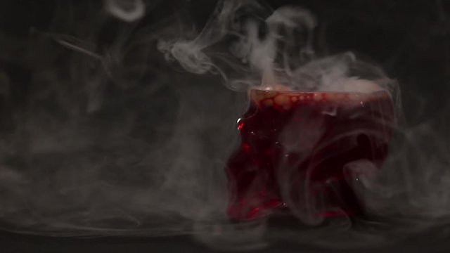 Mystic footage for Halloween for witches or extrasensory. Smoke and bubbles rise in a glass-skull on a dark background.