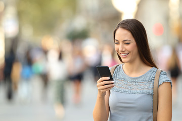 Happy lady using a smart phone standing on the street