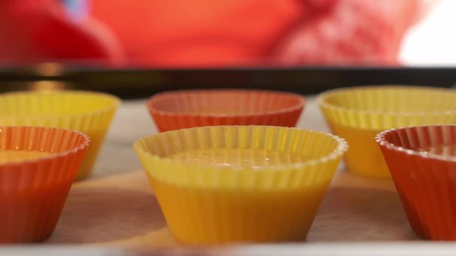 Granny places baking sheet with muffin cupcake silicone molds on rack of the preheated oven. View from inside of the oven. Basic recipe. Making homemade muffins. Quick sweet dessert for breakfast.