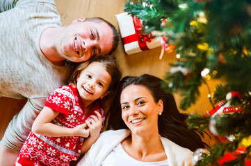 Obraz na płótnie Canvas Young family lying under Christmas tree among presents,
