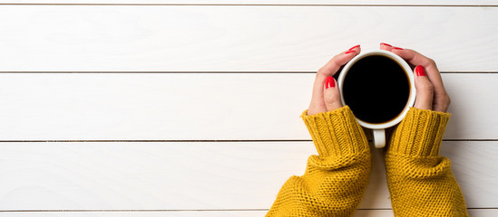 Female hands in warm sweater holding cup of coffee