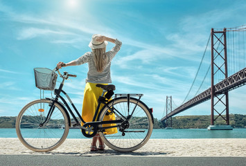 Blonde woman in summer hat and yellow skirt with her city bicycl