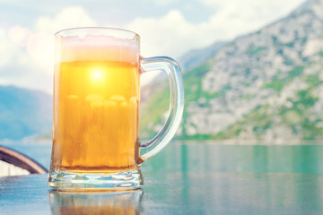 Mug of beer on the background of the sea and mountains in the sunlight