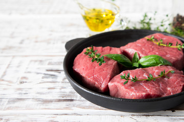 raw beef steak on a light wooden background with olive oil and spices