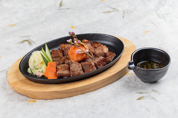 Isolated top view of Garlic Saikoro Steak: medium rare dice wagyu topping with mince carrot on hot plate served with potato salad with ponzu sauce on washi (Japanese paper).