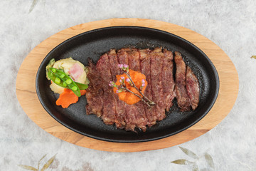 Top view of medium rare wagyu steak topping with mince carrot on hot plate and wooden plate served with potato salad on washi (Japanese paper).