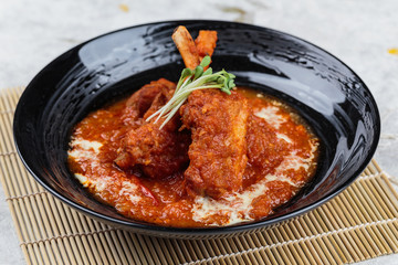 Close-up Pork rib chops steaks boiled with tomato sauce and cheese served in black round plate on makisu (meal mat).