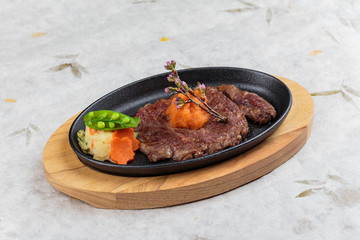 Isolated medium rare wagyu steak topping with mince carrot on hot plate and wooden plate served with potato salad  on washi (Japanese paper).