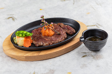 Medium rare wagyu steak topping with mince carrot on hot plate and wooden plate served with potato salad with ponzu sauce on washi (Japanese paper).