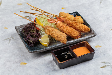 Mix tempura stick (Shrimp, salmon and quail eggs) served with slice cabbage, red oak lettuce and sliced lemon with ponzu and thousand island sauce in stone plate on washi (Japanese paper).
