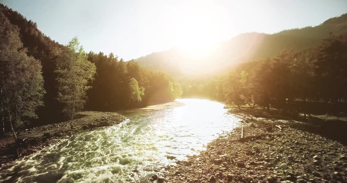 4k (UHD) aerial view. Low flight over fresh cold mountain river at sunny summer morning. Green trees and sun rays.