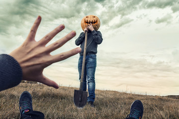 Modern Jack-lantern with  pumpkin on his head and shovel looks at his victim.  Halloween concept.