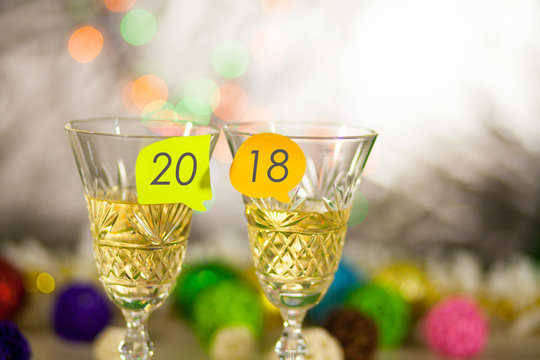 Two glasses with champagne on a table with stickers and an inscription 2018. New Year's bright blurred background