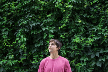 Retrato minimalista de hombre joven con camiseta rosa mirando al cielo y con un frondoso fondo de hojas verdes.