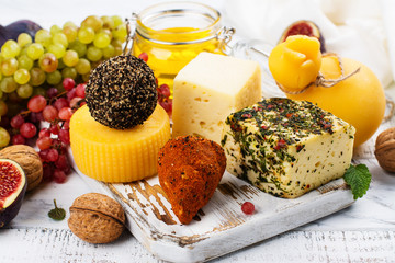 Assortment of farm cheese with supplemental snacks, fruits and nuts on white wooden table