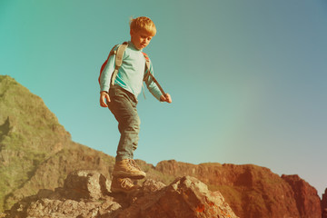 little boy with backpack hiking in mountains