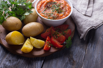 Young potatoes boiled in a peel with zucchini caviar or dip of vegetables, spices, fresh tomatoes and parsley on a wooden board. Simple healthy homemade food