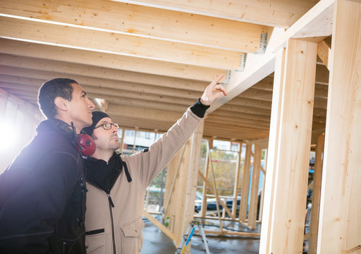 Carpenter Showing Wooden Beams To Colleague At Site