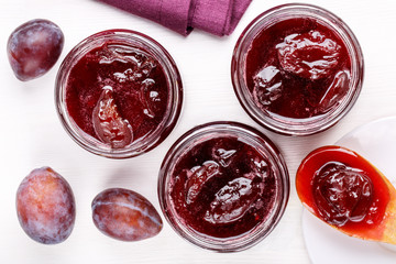 Glass jars of homemade plum jam on white table.