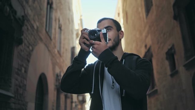 Epic shot of foreign tourist discovering new culture, european city full of historical buildings and landmarks, makes photographs on vintage retro camera, looks around amazed and inspired