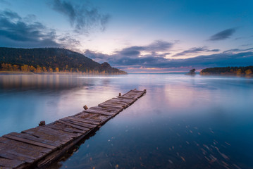 Beautiful morning landscape. Old wooden gangway at foggy Borovoe lake and stone sculprure jumbaktas, Burabay National park in Northern Kazakhstan. Long exposure shot.