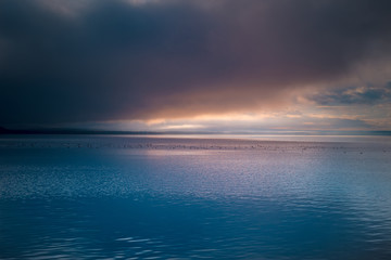 Beautiful sunrise. Dramatic clouds over mountain lake. Ducks on the water surface.