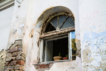 A window in an old ruined house with a tiled texture with a window sill on which stand brown pots with flowers