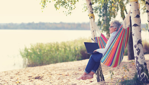 ältere attraktive Frau mit Laptop am See in der Hängematte