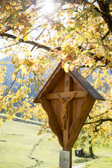 Materl/Holzkreuz mit Jesus, Herbsttag mit bunten Blättern und Sonnenstrahlen