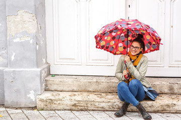 Young female sitting on stairs at the old city downtown.Raining day and autumn concept.