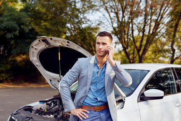Young man stands next to a broken car calling