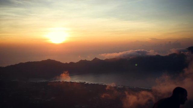 Silhouette of woman taking picture with smart phone camera enjoying sunrise, View from Mount Batur on Volcano Agung and Abang, Bali, Indonesia.