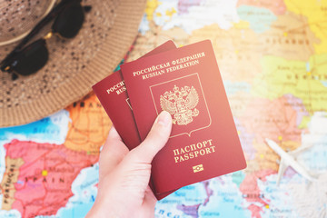 Hand holding international passport on the world map background with hat and model airplane / travel concept/ selective focus
