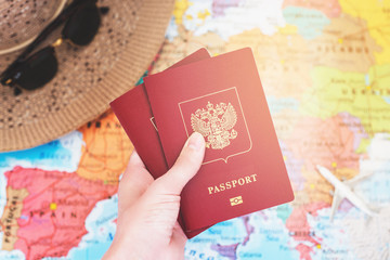 Hand holding international passport on the world map background with hat and model airplane / travel concept/ selective focus