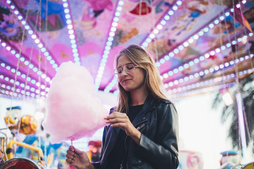 Adorable cute pretty woman stands in middle of amusement park, in front of ride with bright colours...