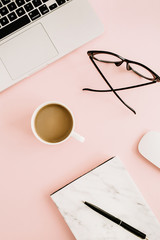Flat lay modern women's workspace with laptop, marble notebook, glasses, mouse and coffee on pastel pink background. Top view.