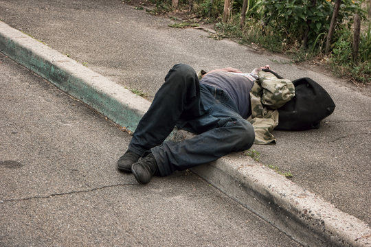 Unconscious drunk man. Person lying in the street. Health problems of the homeless.