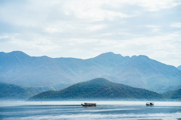 Boats are crossing tranquil lake with mountains landscape. Amazing view at Skadar lake, Montenegro