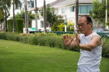 asian senior man wear white shirt stand and practice tai chi on the grass in the garden