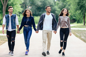 Full-length portrait of young friends holding hands walking in park