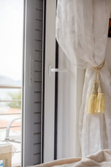 Part of a beautiful curtain, blinds and a terrace with views. Beautiful white curtain with accessory. Close up of piled curtain.