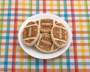 A plate full of football shaped sugar cookies with sprinkles on a colorful place mat.