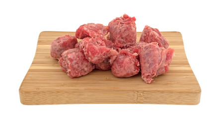 Several slices of raw mild bratwurst sausage on a wood cutting board isolated on a white background.