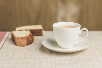 Cup of tea with two bread on tablecloth and wooden background
