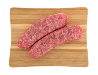 Top view of two mild bratwurst sausages on a wood cutting board isolated on a white background.
