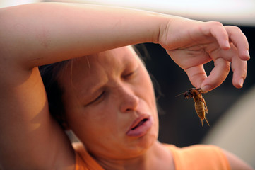 The girl looks at the hideous insect a bear-like mole in the summer noon in the village courtyard