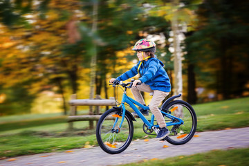 Cute child, boy riding bike in autumn park, afternoon